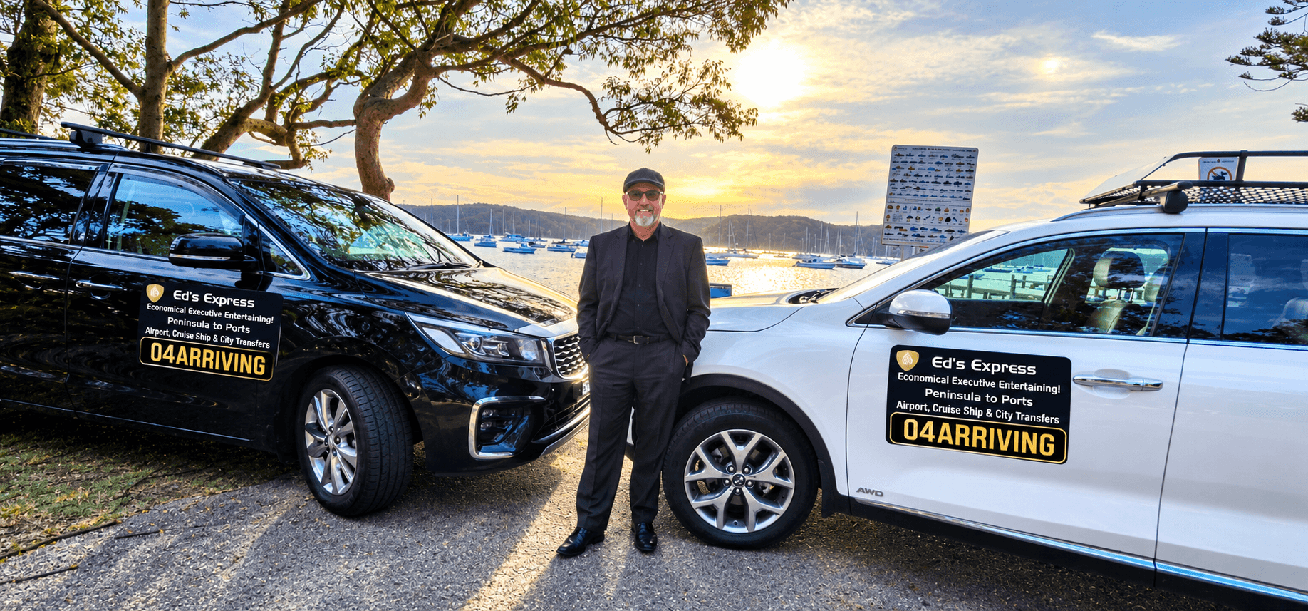 Chauffeur standing between black and white branded Ed's Express cars by the waterfront at sunset.